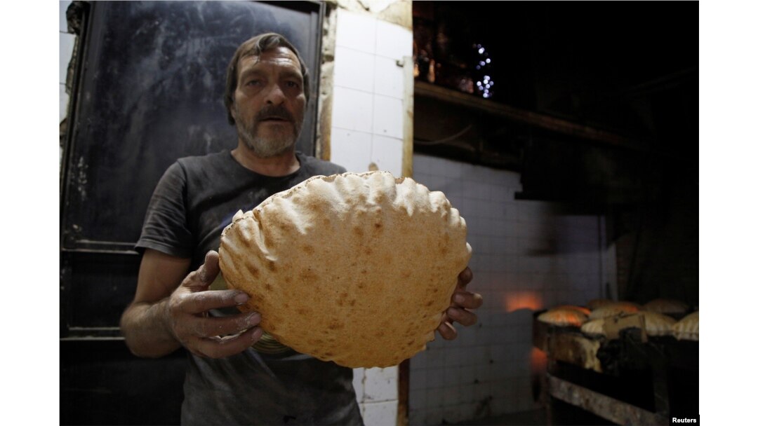 A man poses with a loaf of bread inside a government bakery in Damascus, Syria, Sept. 17, 2016.