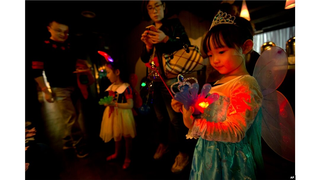 FILE - a girl plays with an electronic toy while standing with her family at a Mother's Day-themed disco dance party for children in Beijing.