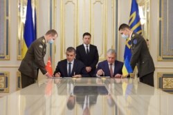 Ukraine's President Volodymyr Zelenskiy looks on while Defense Minister Andriy Taran and CEO of the Turkish defense technology company Baykar Haluk Bayraktar sign a memorandum to establish joint training and maintenance centers for Turkish armed drones, in Kyiv, Sept. 29, 2021.