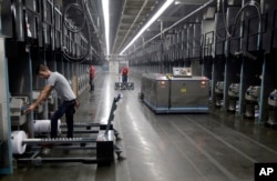 Workers exchange spools of thread as a robot picks up thread made from recycled plastic bottles at a processing center for a textile company in Yadkinville, North Carolina.