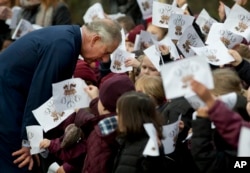 Schoolchildren wave images of the heraldic cypher of Britain's Prince Charles, as he bends down to talk to some of them, after he made a visit to meet Iraqi Christians in London, Dec. 9, 2014.