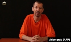 An image taken from a video released by the Islamic State (IS) group through Al-Furqan Media via YouTube allegedly shows British freelance photojournalist, John Cantlie, at an undisclosed location in which he says he is being held captive, Sept. 18, 2014.