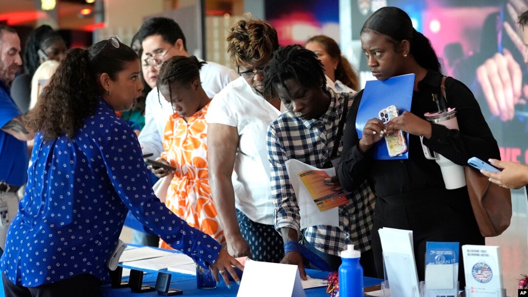 ARCHIVO - Carolina Wilson, del Servicio Postal de los Estados Unidos, a la izquierda, habla con posibles solicitantes de empleo en una feria de empleo, el 29 de agosto de 2024, en Sunrise, Florida.