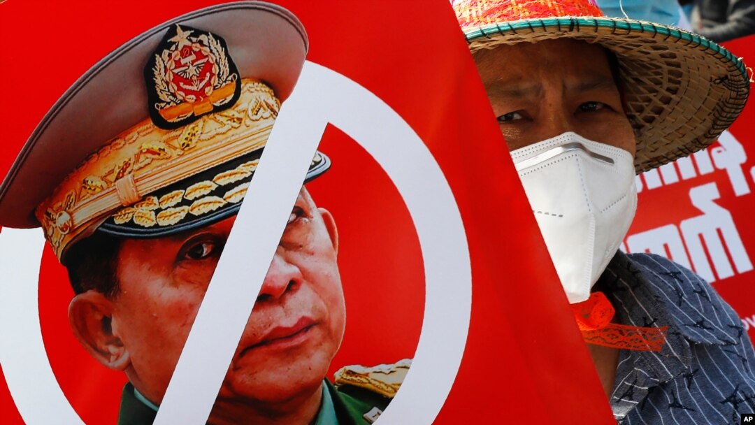 FILE - A protester holds a placard with a crossed out face of Commander in Chief, Senior Gen. Min Aung Hlaing, during an anti-coup rally in front of the Myanmar Economic Bank in Mandalay, Myanmar, Feb. 15, 2021.