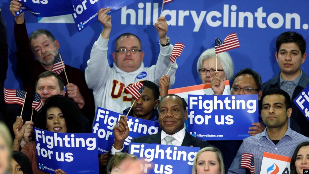 FILE - Supporters of Democratic presidential candidate Hillary Clinton hold signs and flags, March 22, 2016, during a campaign rally at Rainier Beach High School in Seattle, Wash.