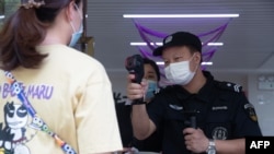 FILE - A security guard checks the body temperature of a woman in Wuhan in China's central Hubei province, May 11, 2020.