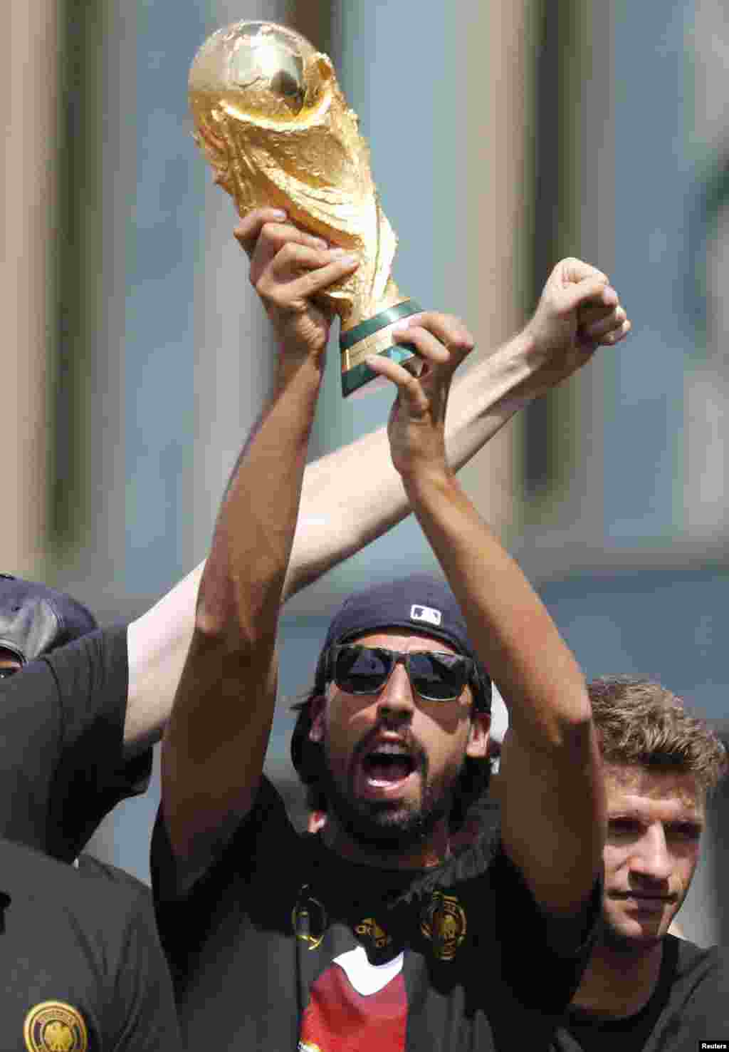 Germany's national soccer team player Sami Khedira lifts up the World Cup trophy on stage during celebrations to mark the team's 2014 Brazil World Cup victory, at the Fan Mile public viewing zone in Berlin, July 15, 2014.