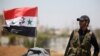 A Syrian army soldier stands next to a Syrian flag in Umm al-Mayazen, in the countryside of Daraa, Syria, July 10, 2018. 