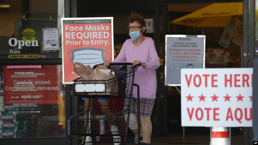 A shopper wearing a mask for protection against COVID-19 leaves a grocery store that is also serving as an early polling site, July 9, 2020, in Austin, Texas.