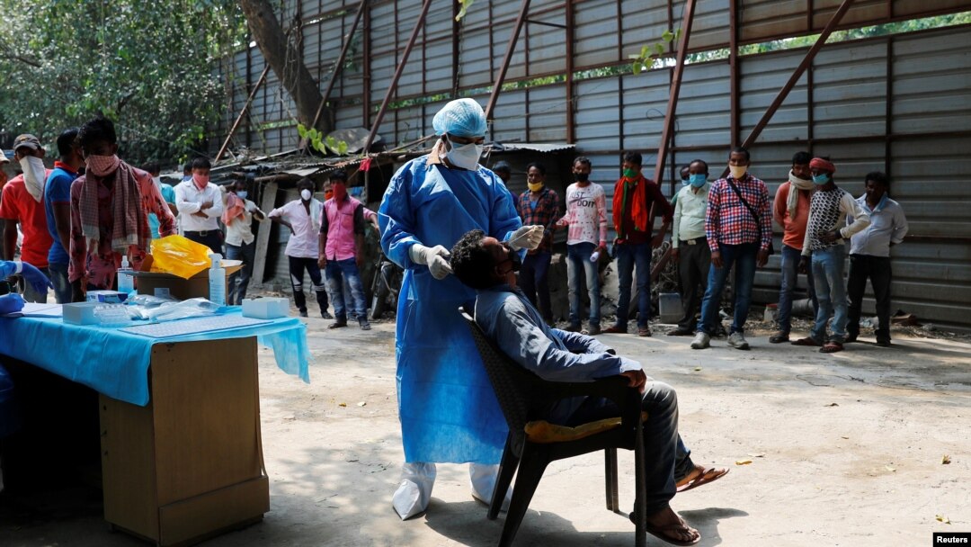 A healthcare worker wearing personal protective equipment (PPE) takes a swab from a migrant laborer for a rapid antigen test at the site of an under construction residential complex in New Delhi, India, Sept. 19, 2020.