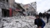 FILE - People walk past debris following airstrikes by government forces, in the town of Ariha, Idlib province, Syria, Jan. 15, 2020. 