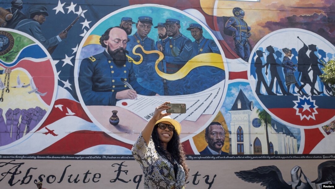 ARCHIVO - Mikia Cain se toma una selfie frente al mural "Igualdad absoluta", que marca el lugar donde un general de la Unión emitió una orden en 1865 que condujo a la libertad de los esclavos en Texas, durante la celebración de Juneteenth en Galveston, el 19 de junio de 2023.