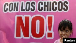 A child stands next to a sigN reading: 'No with the children' during a protest against child abuse and violence in Lima, Peru, Feb. 8, 2018.