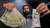 FILE - A money changer poses for the camera with a U.S hundred dollar bill (R) and the amount being given when converting it into Iranian rials (L), at a currency exchange shop in Tehran's business district, Iran, Jan. 20, 2016.