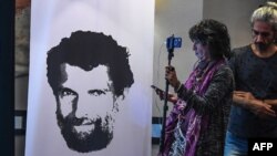 FILE - A journalist stands in front of a poster featuring jailed philanthropist Osman Kavala, during a press conference given by his lawyers, in Istanbul, Turkey, Oct. 31, 2018.