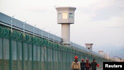 FILE: Workers walk by the perimeter fence of what is officially known as a vocational skills education center in Dabancheng in Xinjiang Uighur Autonomous Region, China, Sept. 4, 2018.