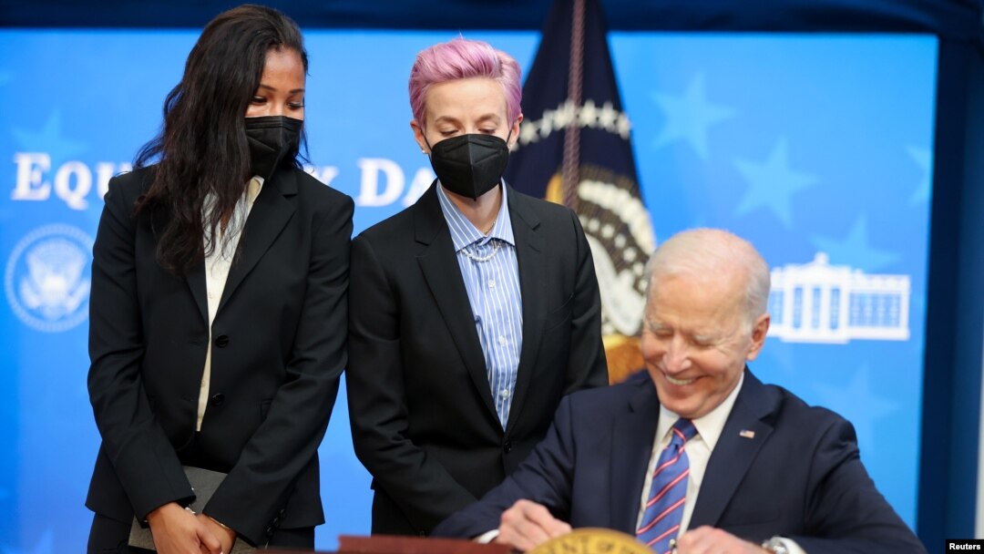 El presidente Joe Biden firma una proclamación con motivo del Día del Salario Equitativo, ante la mirada de las futbolistas Margaret Purce, a la izquierda, y Megan Rapinoe, en la Casa Blanca, el 24 de marzo de 2021.