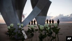 Men in a vintage US WWII uniforms stand behind flowers left at Les Braves monument after a D-Day 76th anniversary ceremony in Saint Laurent sur Mer, Normandy, France, June 6, 2020.