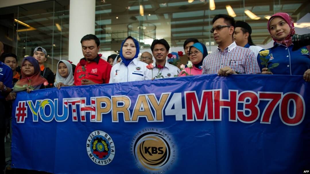Members of a youth group holds roses and a banner as they pray for the missing Malaysia Airlines Boeing 777-200 plane at a hotel in Putrajaya on March 10, 2014. 