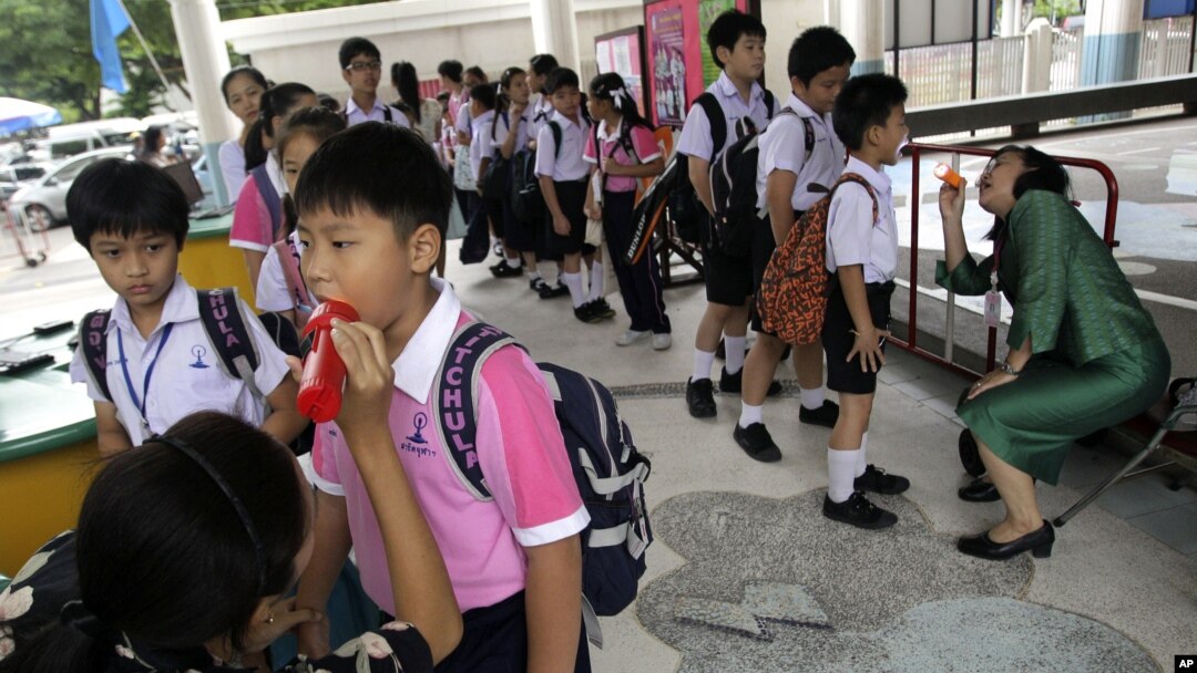 Thai teachers check the mouth of the students for hand, foot and mouth disease, before they get inside the school in Bangkok, July 25, 2012. 