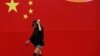 FILE - A woman wearing a mask walks past a wall painted with China's national flag in central Beijing.