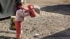 FILE - A girl drinks water in the street outside her tent at a camp for internally displaced people in western Baghdad, Iraq, Feb. 1, 2018. 