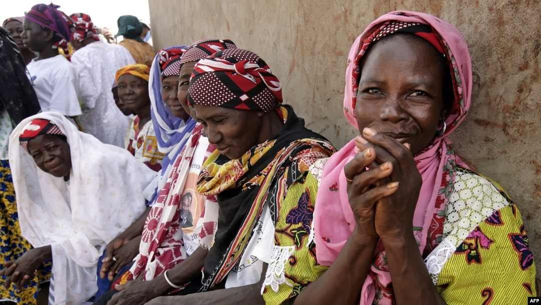 FILE - Women wait outside the workroom of the Multi-functional Platform for Poverty Alleviation in the village of Poa near Ougadougou in Burkina Faso.