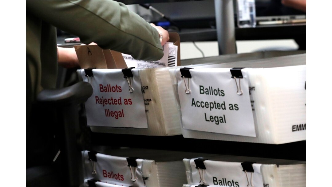 FILE - A Miami-Dade County Elections Department employee places a vote-by-mail ballot for the August 18 primary election into a box for rejected ballots at the Miami-Dade County Elections Department, in Doral, Florida, July 30, 2020.