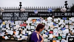 A woman passes a fence outside Brooklyn's Green-Wood Cemetery adorned with tributes to victims of COVID-19, Thursday, May 28, 2020, in New York. The memorial is part of the Naming the Lost project which attempts to humanize the victims who are often…