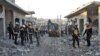 Members of the Syrian Civil Defense, also known as the White Helmets, stand with an excavator in a street filled with rubble and debris following a reported airstrike in the village of Balyun in Syria's northwestern Idlib province, Dec. 7, 2019.